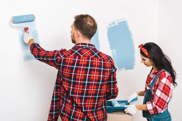 Hombre y mujer pintando pared en color azul en casa - foto de stock