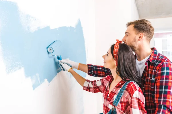 Allegro uomo e donna pittura parete in colore blu a casa — Foto stock