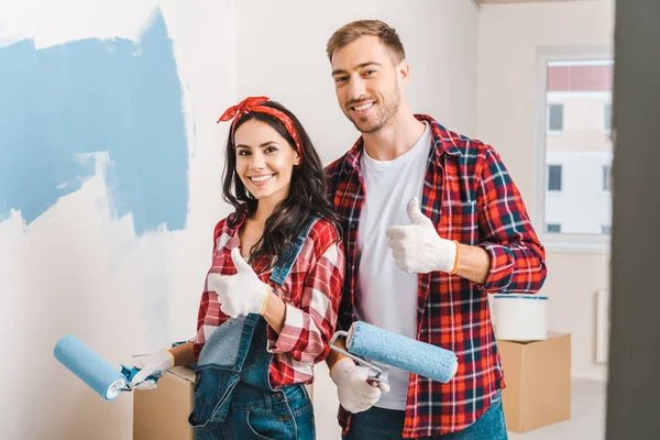 Homme et femme joyeux montrant pouces levés tout en tenant des rouleaux dans les mains — Photo de stock