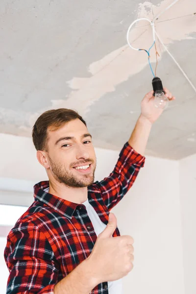 Fröhlicher Mann wechselt Glühbirne und zeigt Daumen hoch — Stockfoto