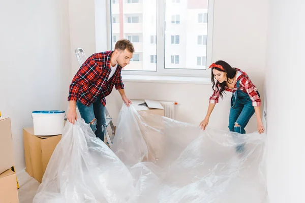 Quarto de cobertura casal feliz com polietileno em casa — Fotografia de Stock