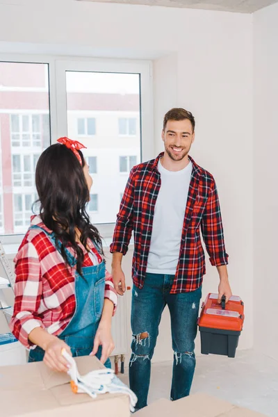 Enfoque selectivo del hombre alegre mirando a la mujer mientras sostiene la caja de herramientas - foto de stock