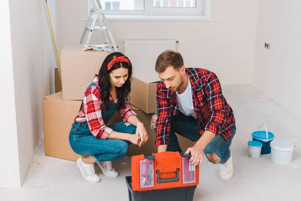 Hombre y mujer sentados y mirando la caja de herramientas en casa - foto de stock