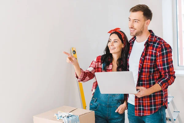 Attrayant femme pointant du doigt tout en se tenant debout avec petit ami tenant ordinateur portable — Stock Photo