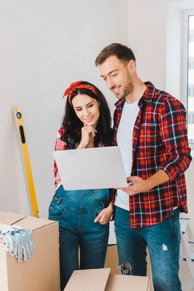 Cheerful woman standing with boyfriend and looking at laptop — Stock Photo