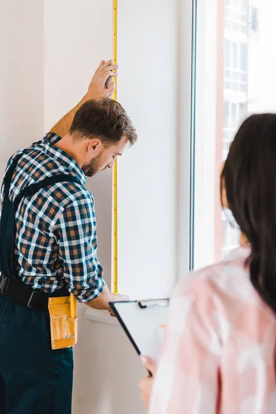 Handyman measuring window with measuring tape near female client — Stock Photo