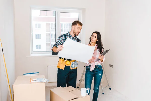 Cheerful handyman holding blueprint near attractive client — Stock Photo