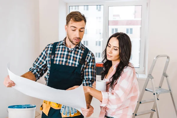 Bello handyman tenendo cianografia vicino donna attraente — Foto stock