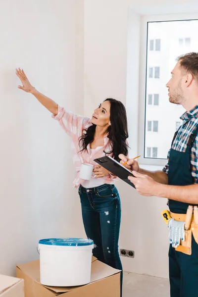 Selektiver Fokus der attraktiven Frau, die dem Handwerker die Wand zeigt — Stockfoto