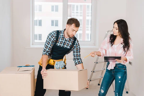 Attraktive Frau zeigt auf Schachtel in den Händen eines Handwerker — Stockfoto