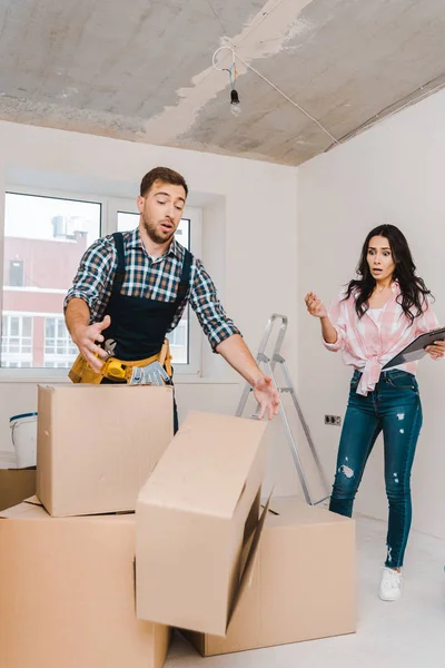 Femme surprise regardant tomber boîte près beau bricoleur — Photo de stock