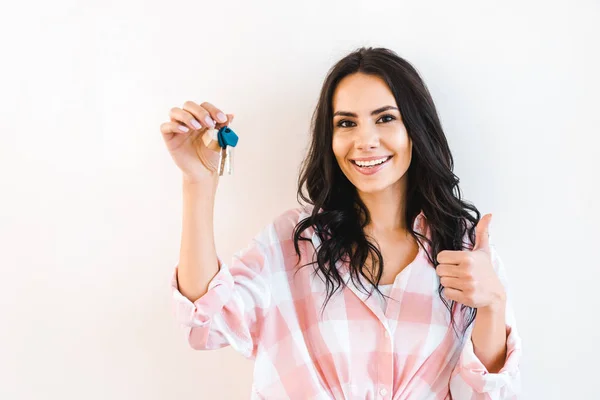 Cheerful woman holding key while showing thumb up isolated on white — Stock Photo