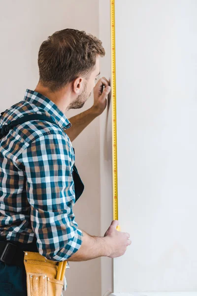 Handwerker steht und misst Wand mit Maßband — Stockfoto