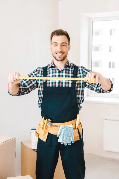 Cheerful handyman smiling while holding measuring tape — Stock Photo