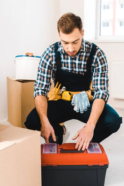 Serious handyman sitting near toolbox in room — Stock Photo