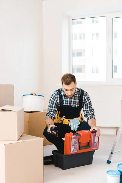 Serious handyman sitting and looking at toolbox in room — Stock Photo