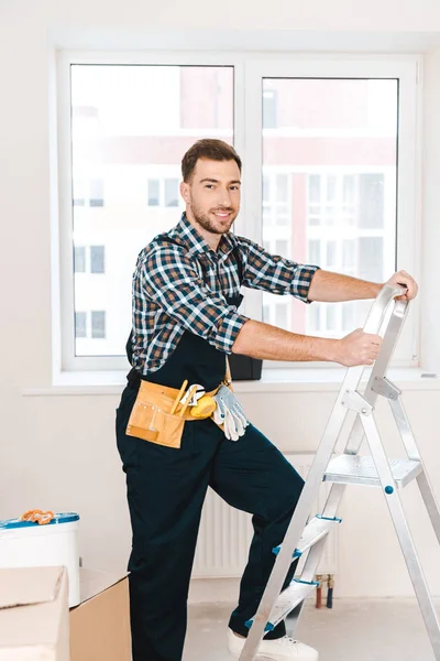 Fröhlicher Handwerker, der neben der Leiter steht und im Zimmer lächelt — Stockfoto