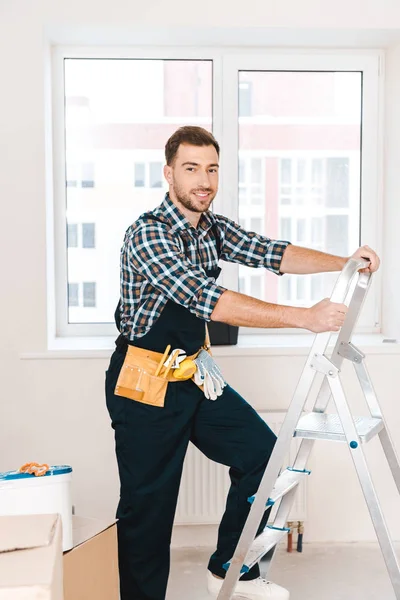 Manitas alegres de pie cerca de la escalera y sonriendo en la habitación - foto de stock