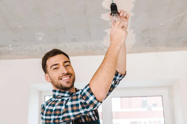 Fröhlich gutaussehender Handwerker wechselt Glühbirne aus Glas — Stockfoto