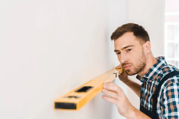 Foco seletivo de handyman bonito segurando nível de medição perto da parede — Fotografia de Stock