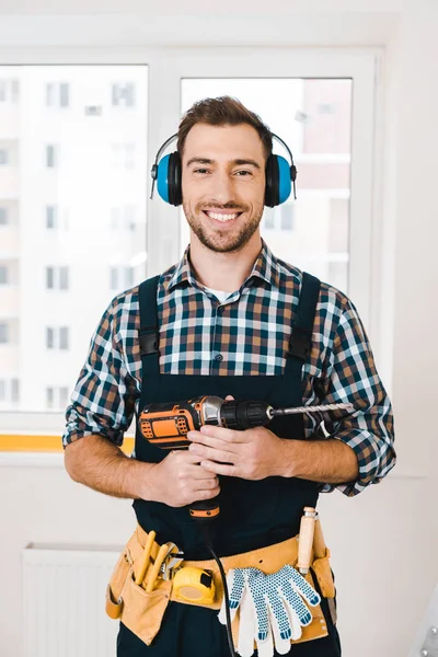 Handsome handyman smiling while holding drill in hands — Stock Photo