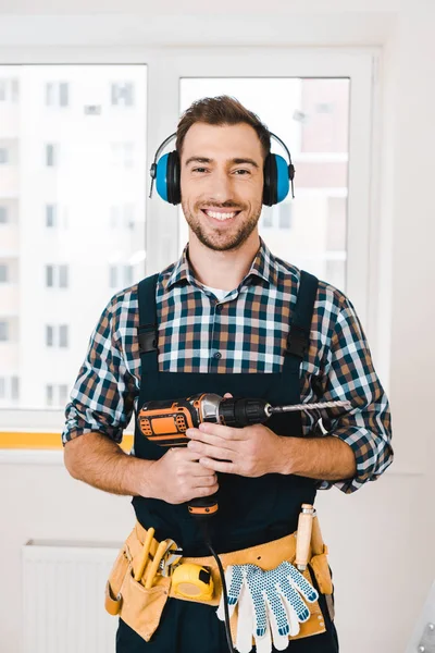 Schöner Handwerker lächelt, während er den Bohrer in den Händen hält — Stockfoto