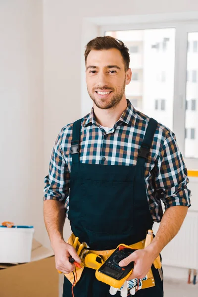 Schöner Handwerker lächelt, während er digitale Multimeter in der Hand hält — Stockfoto