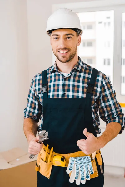 Cheerful handyman holding wrench and showing thumb up — Stock Photo