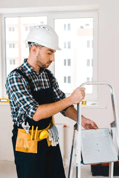 Guapo manitas en casco sosteniendo escalera en la habitación - foto de stock