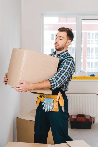 Guapo handyman celebración caja mientras está de pie en la habitación - foto de stock