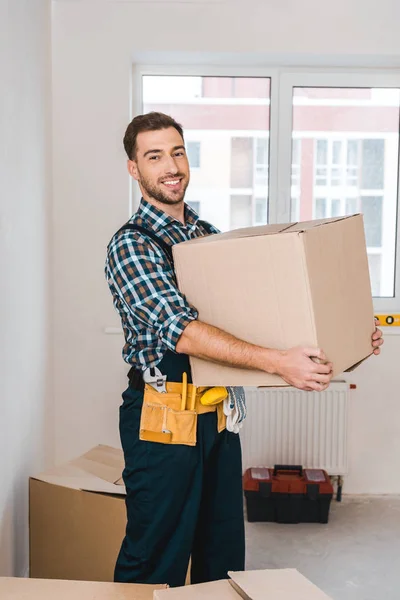 Cheerful handyman holding box while standing in room — Stock Photo