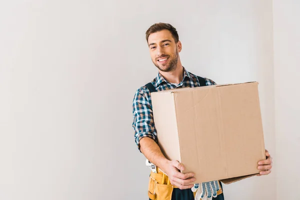 Feliz handyman segurando caixa enquanto está perto da parede — Fotografia de Stock