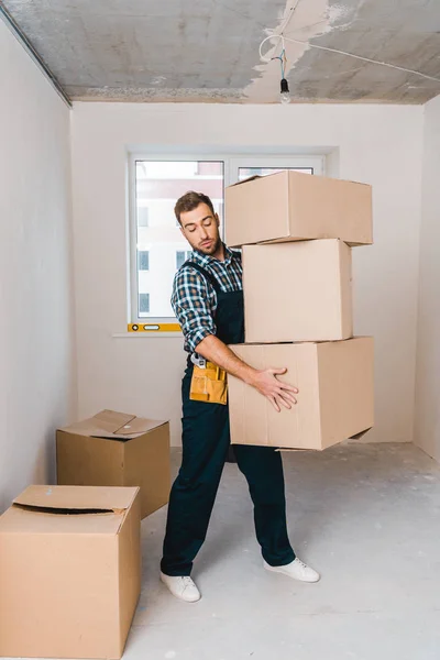Bello handyman tenere scatole mentre in piedi in camera — Foto stock