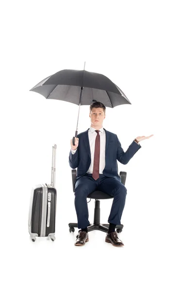 Бизнесмен, сидящий на стуле с зонтиком и багажом для деловой поездки, изолированный на белом — стоковое фото