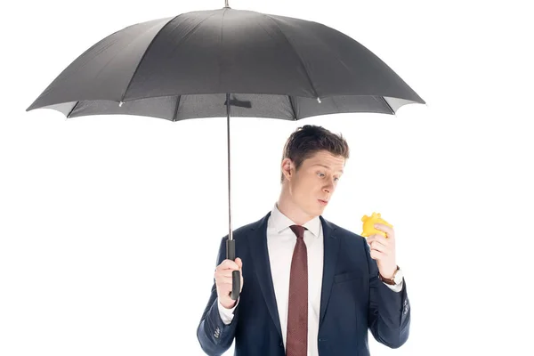 Jeune homme d'affaires avec parapluie regardant petite tirelire isolé sur blanc — Photo de stock