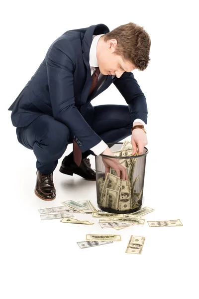 Young businessman taking money from trash can on white — Stock Photo