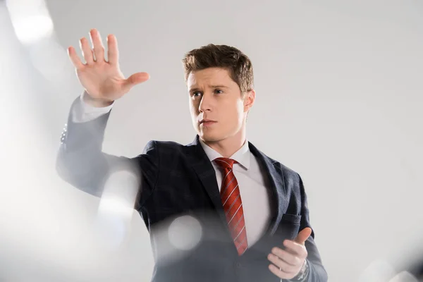 Selective focus of young businessman gesturing and touching something on grey — Stock Photo