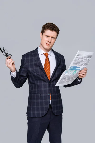 Молодий бізнесмен тримає окуляри і газети ізольовані на сірому — стокове фото