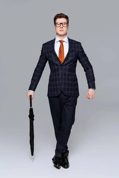 Guapo hombre de negocios elegante posando con paraguas aislado en gris - foto de stock