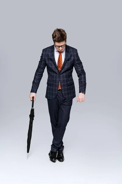 Stylish businessman in suit posing with umbrella isolated on grey — Stock Photo