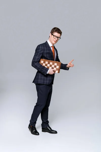Молодий бізнесмен вказує і тримає шахову дошку ізольовано на сірому — стокове фото