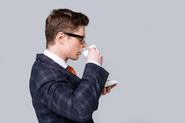 Vista lateral de hombre de negocios guapo en traje de moda beber café aislado en gris - foto de stock
