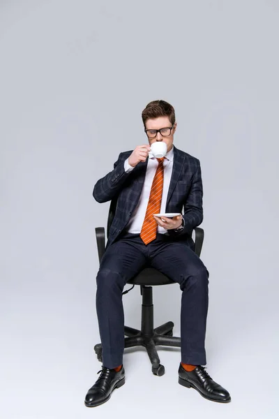 Homem de negócios elegante sentado na cadeira e beber café em cinza — Fotografia de Stock