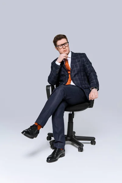 Elegante hombre de negocios reflexivo sentado en la silla en gris - foto de stock