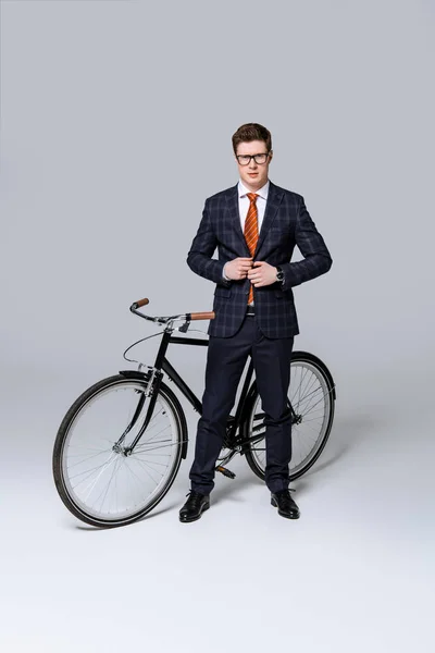 Homme d'affaires élégant en tenue formelle posant avec vélo sur gris — Photo de stock