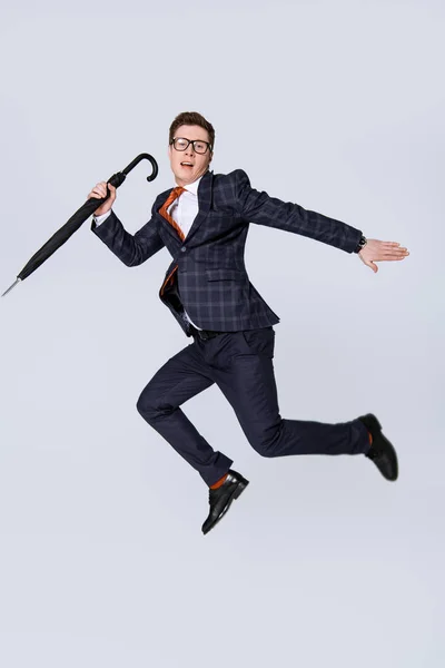Stylish young businessman jumping with umbrella isolated on grey — Stock Photo