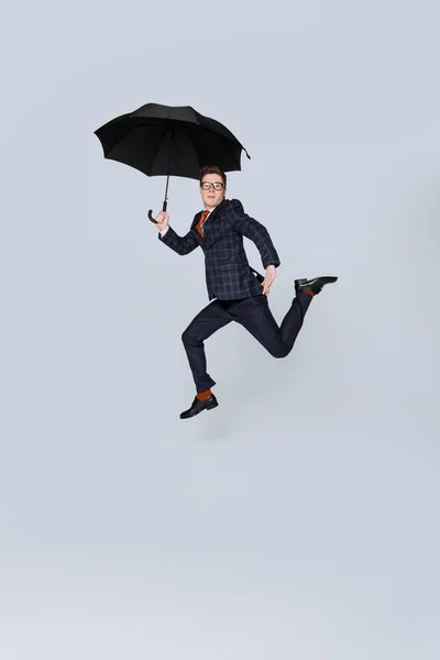 Homem de negócios elegante em terno pulando com guarda-chuva isolado em cinza — Fotografia de Stock