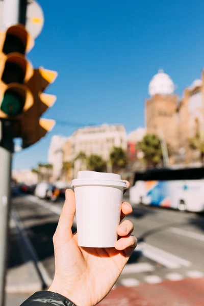 Enfoque selectivo de la mano masculina con taza de papel, escena urbana sobre fondo, barcelona, España - foto de stock