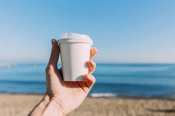 Vue partielle de l'homme tenant une tasse en papier sur fond bleu tranquille de la mer, Barcelone, Espagne — Photo de stock