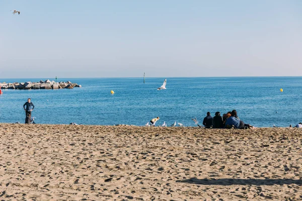 BARCELONA, ESPAÑA - 28 DE DICIEMBRE DE 2018: vista panorámica del mar y personas sentadas en la playa - foto de stock